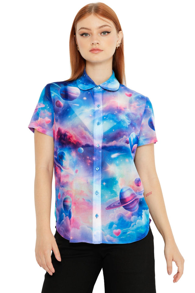 Model wearing a pastel galaxy button-up shirt with planets, clouds and pink heart details on a blue sky background.